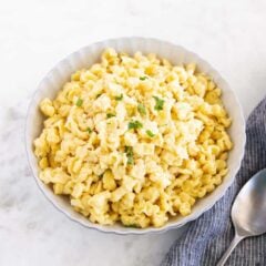 Bowl of German spaetzle topped with parmesan and parsley, served beside a spoon and kitchen towel.