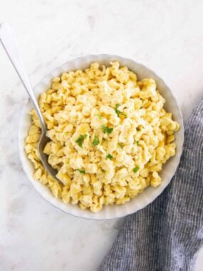 Overhead view of homemade German spaetzle in a white serving bowl topped with parmesan and parsley.