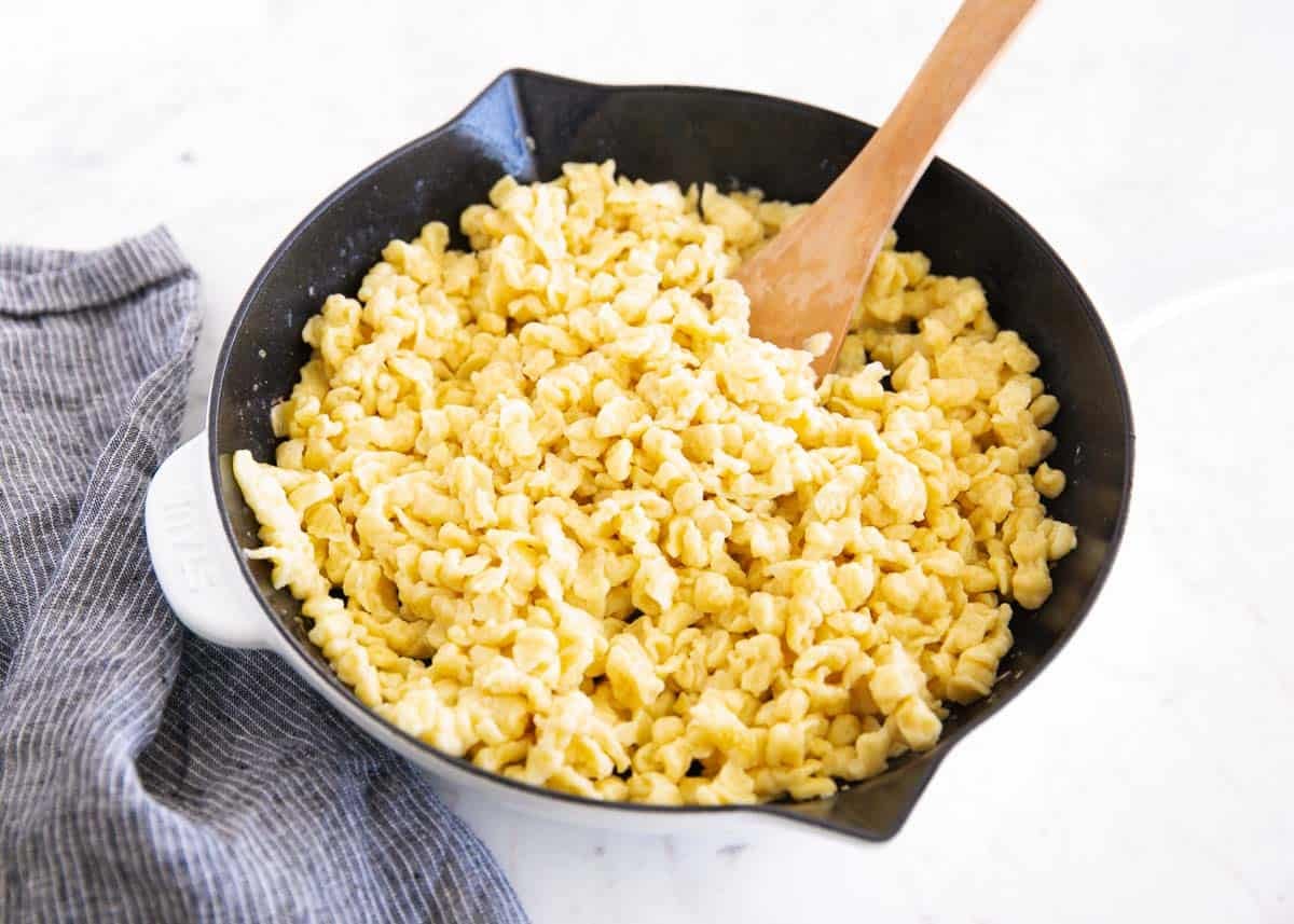 Learn to make homemade German spaetzle that's soft, chewy, and on the table in under 30 minutes. So good with brown butter, gravy, or cheese. Freshly cooked German spaetzle in a black skillet with a wooden spoon.