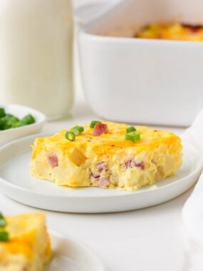 A square slice of Amish breakfast casserole garnished with sliced green onions on a white plate.