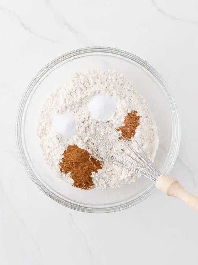 Whisking together the flour, baking soda, salt, cinnamon, and nutmeg in a bowl.
