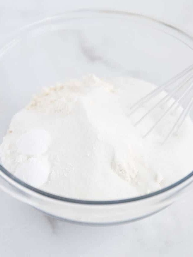Whisking dry muffin ingredients in a glass bowl.
