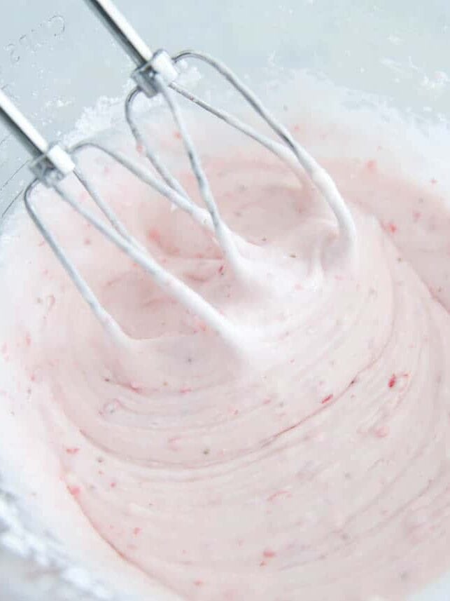 Mixing strawberry cream cheese frosting in bowl to top strawberry sheet cake.
