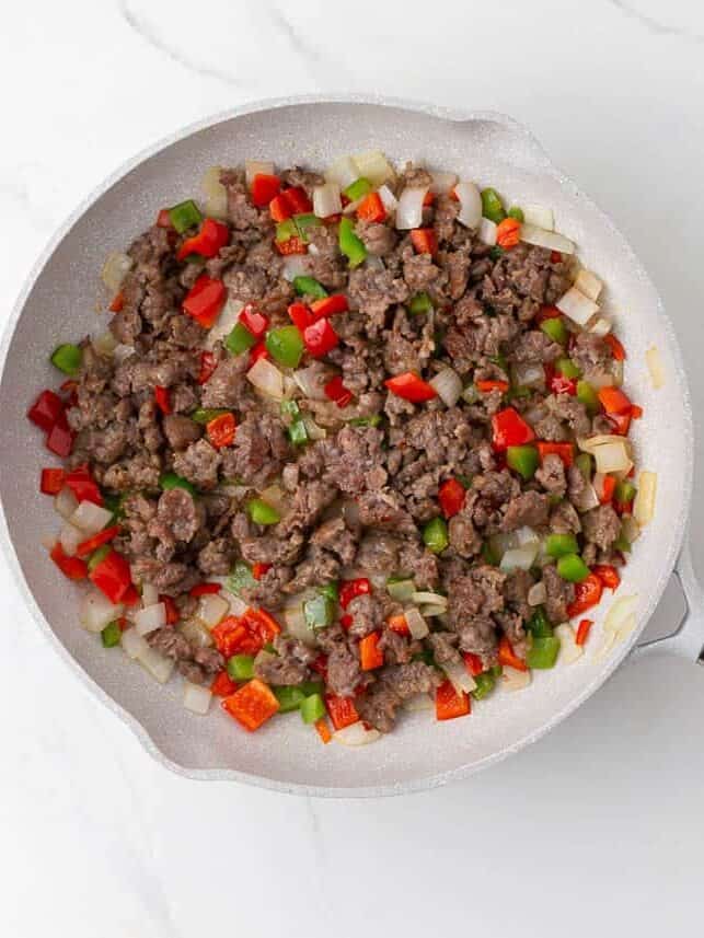Browned breakfast sausage with saut&eacute;ed onions and bell peppers in a skillet.