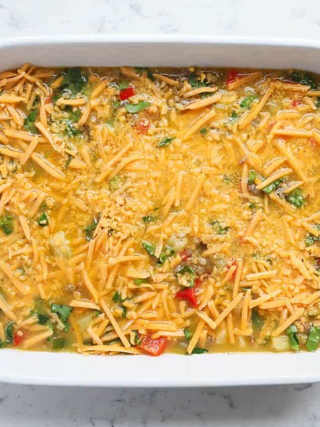 Unbaked breakfast casserole topped with shredded cheddar cheese ready to refrigerate overnight.