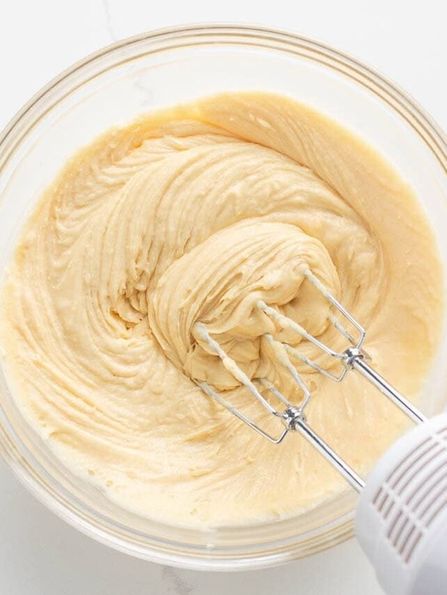 Almond cake batter being mixed with a hand mixer in a glass bowl.