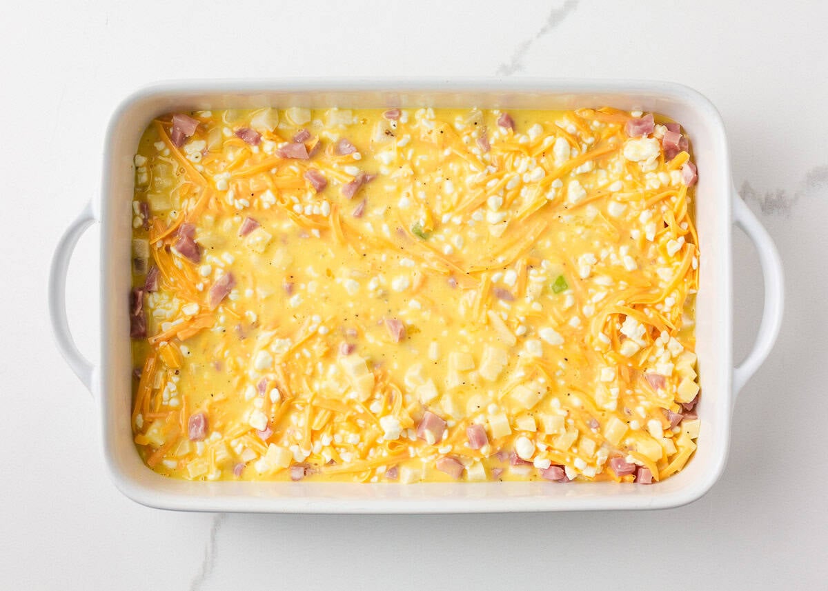 Overhead view of a white baking dish filled with the unbaked egg, cheese, ham, and potato mixture, ready to go into the oven.