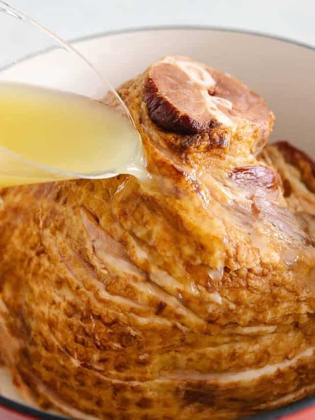 Pouring pineapple juice over ham in a Dutch oven to keep it moist while baking.