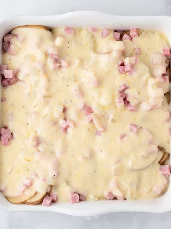 Unbaked scalloped potatoes and ham covered in homemade creamy cheese sauce ready for the oven.