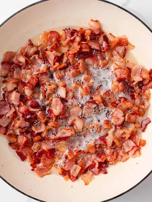 Packed with bold flavors in every bite, this cowboy pasta salad is made with tender noodles, bacon, seasoned ground beef, a creamy dressing, and Southwestern flavor! Chopped bacon cooking in a large white Dutch oven, sizzling in rendered fat until crispy.