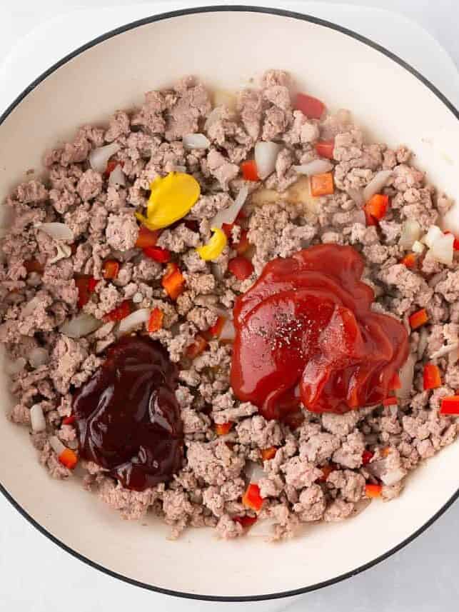 Sloppy joes sauce ingredients added to browned ground beef with diced onions and red peppers in a pot.