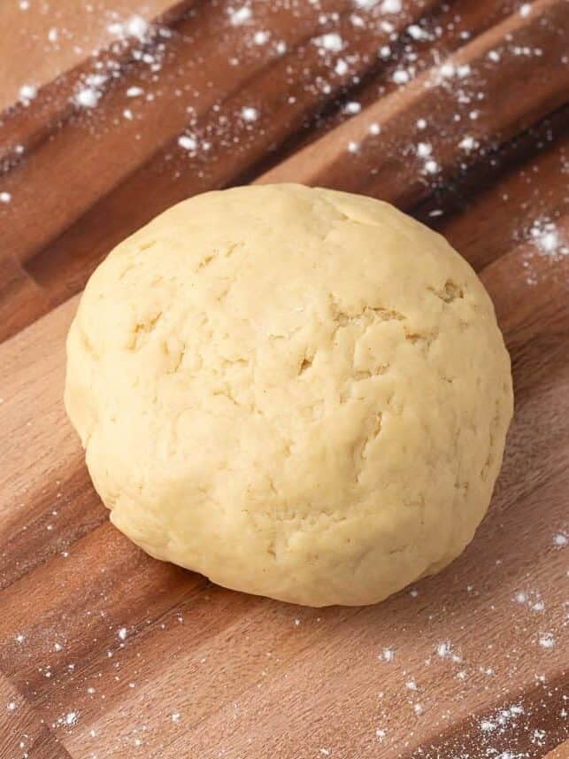 Ball of homemade empanada dough on a floured wooden cutting board.