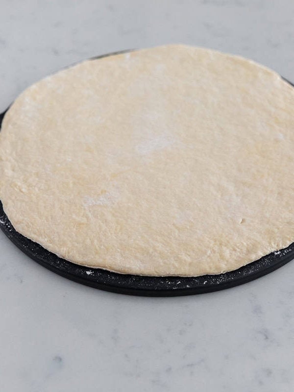 No yeast pizza dough rolled out into a round crust on a black pizza pan.