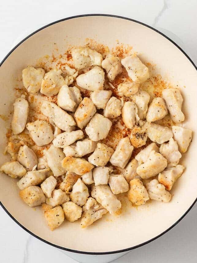 This pineapple chicken is sweet, tangy, and on the table in 30 minutes. Tender chicken, crisp bell peppers, and juicy pineapple in a sauce that beats takeout every time. Overhead view of seasoned chicken breast pieces cooked until golden in a white skillet.