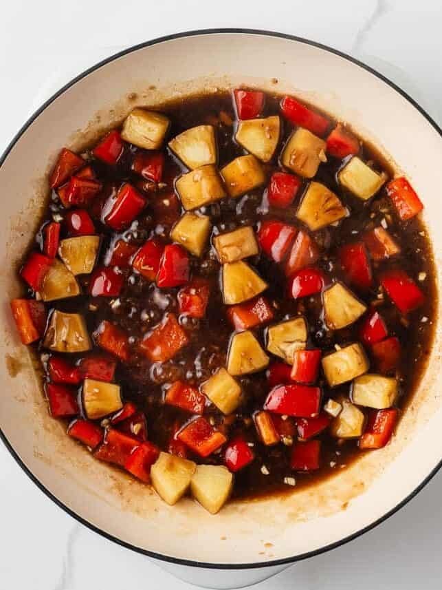This pineapple chicken is sweet, tangy, and on the table in 30 minutes. Tender chicken, crisp bell peppers, and juicy pineapple in a sauce that beats takeout every time. Overhead view of pineapple chunks and red bell pepper simmering in a pineapple soy sauce in a white skillet.