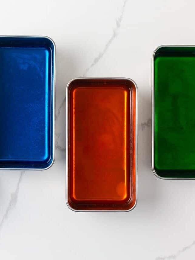 Made with Jello and sweetened condensed milk, stained glass jello has a fun, brightly colored, broken glass look and is the perfect make-ahead dessert for all your parties! Four small loaf pans filled with set Jell-O in red, blue, orange, and green, ready to be cut into cubes for stained glass jello.