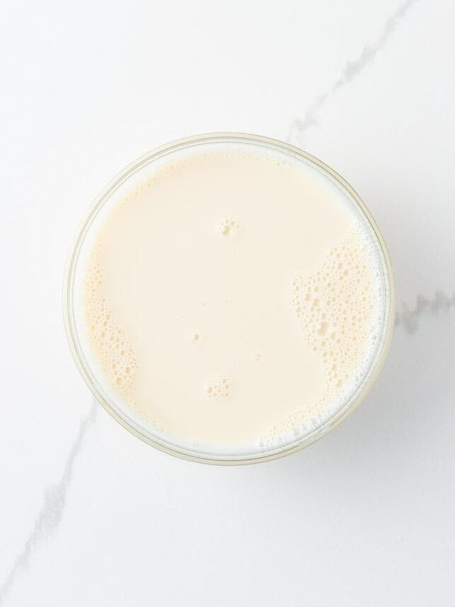 Made with Jello and sweetened condensed milk, stained glass jello has a fun, brightly colored, broken glass look and is the perfect make-ahead dessert for all your parties! Overhead view of a glass bowl filled with the creamy sweetened condensed milk and gelatin mixture used as the white base for rainbow stained glass jello.