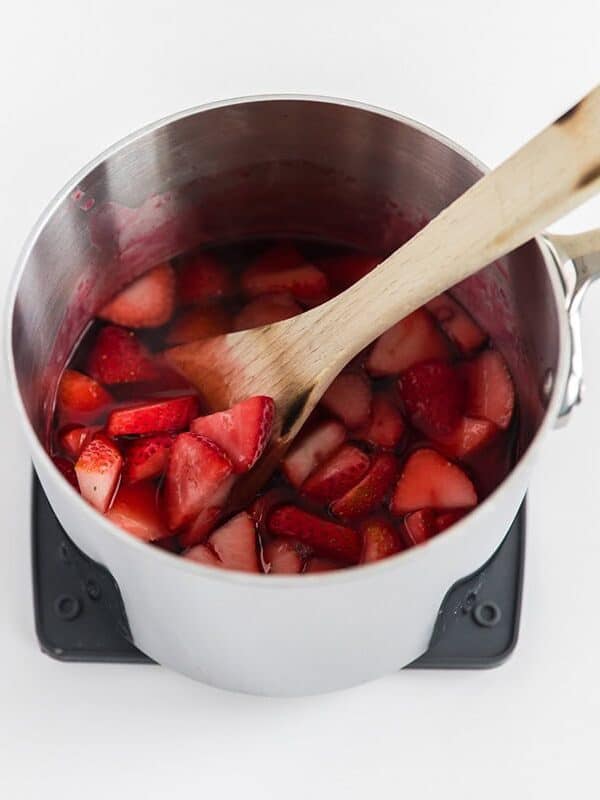 Fresh strawberries stirred into dissolved strawberry Jell-O in a saucepan for pretzel salad topping.