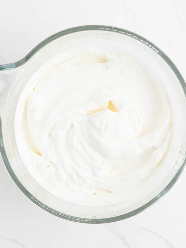 Stabilized whipped cream beaten to stiff peaks in a glass mixing bowl.