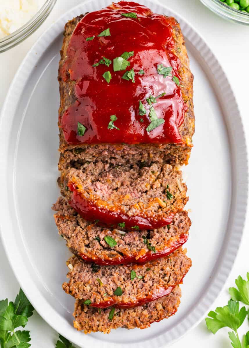 This super simple sweet and tangy meatloaf sauce comes together in minutes with just 3 ingredients! It's the ultimate topping and the perfect finish to all your favorite meatloaf recipes! Sliced meatloaf topped with sweet and tangy meatloaf glaze on a white oval platter.