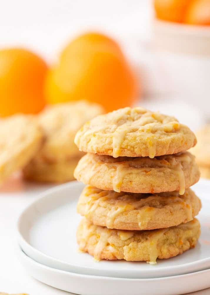 Stack of orange creamsicle cookies with orange glaze on a white plate, soft and chewy with visible orange zest.