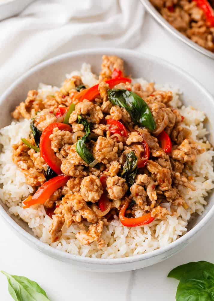This easy Thai basil chicken recipe is bold, savory, and ready in under 30 minutes. It's everything you love about your favorite Thai food, made right at home! Close-up of Thai basil chicken with ground chicken, basil leaves, and red chili peppers in skillet.