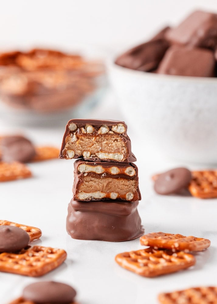 If you love Take 5 candy bars, you are going to love this easy homemade version. No baking required and every bite is the perfect mix of salty, sweet, and crunchy. Close-up side view of three chocolate-dipped pretzel bites stacked on top of each other, with the top one cut in half to show layers of peanut butter filling, caramel, and pretzels inside.