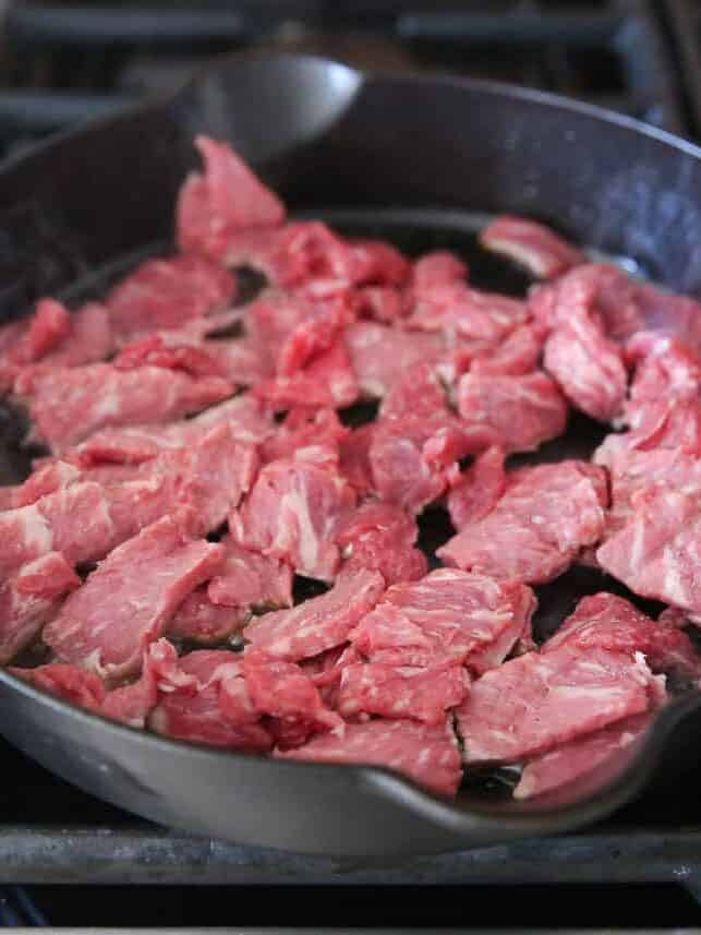 Sliced ribeye steak in a black cast iron skillet on a gas stovetop.