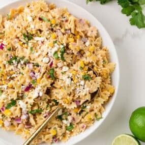 Mexican street corn pasta salad with bow tie pasta, charred corn, cotija cheese, cilantro, and creamy chili lime dressing in a white bowl.