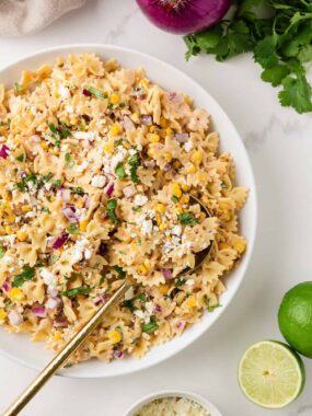 Mexican street corn pasta salad with bow tie pasta, charred corn, cotija cheese, cilantro, and creamy chili lime dressing in a white bowl.