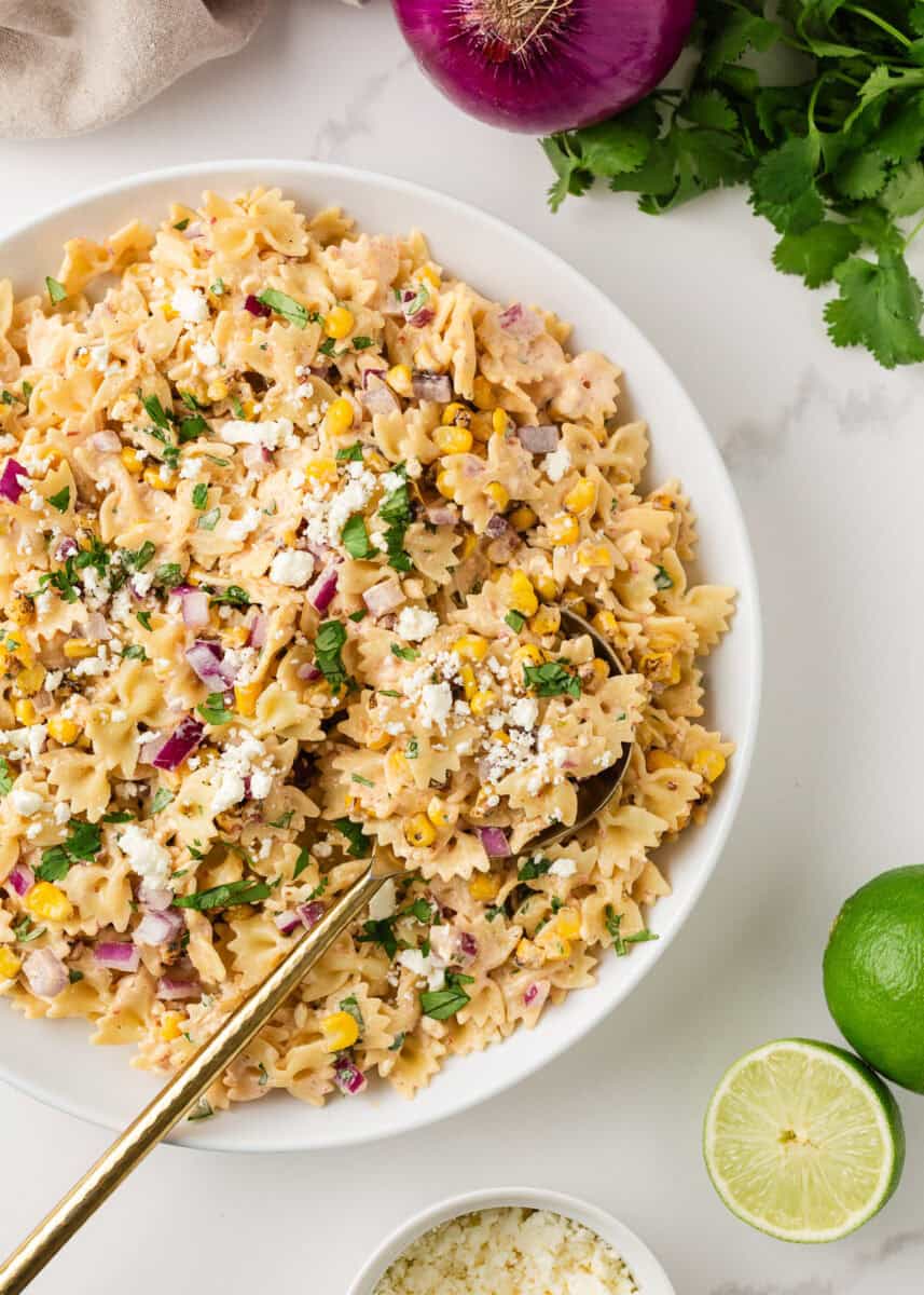 Mexican street corn pasta salad with bow tie pasta, charred corn, cotija cheese, cilantro, and creamy chili lime dressing in a white bowl.