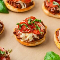 Close-up of mini open-faced pizza burgers with melted cheese, pepperoni slices, and fresh basil on toasted buns.