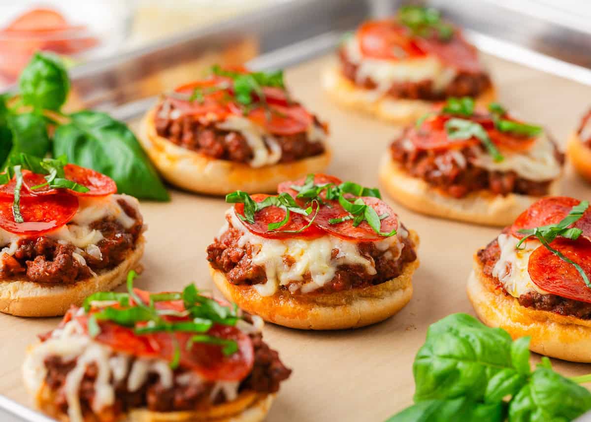 Open-faced pizza burgers with seasoned ground beef, melted mozzarella, pepperoni, and fresh basil on toasted buns.