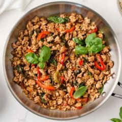 Thai basil chicken (pad krapow gai) in a skillet with ground chicken, red peppers, and fresh basil.