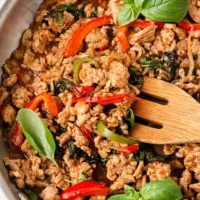 Close-up of Thai basil chicken with ground chicken, basil leaves, and red chili peppers in skillet.