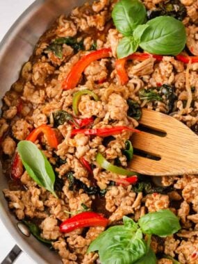 Close-up of Thai basil chicken with ground chicken, basil leaves, and red chili peppers in skillet.