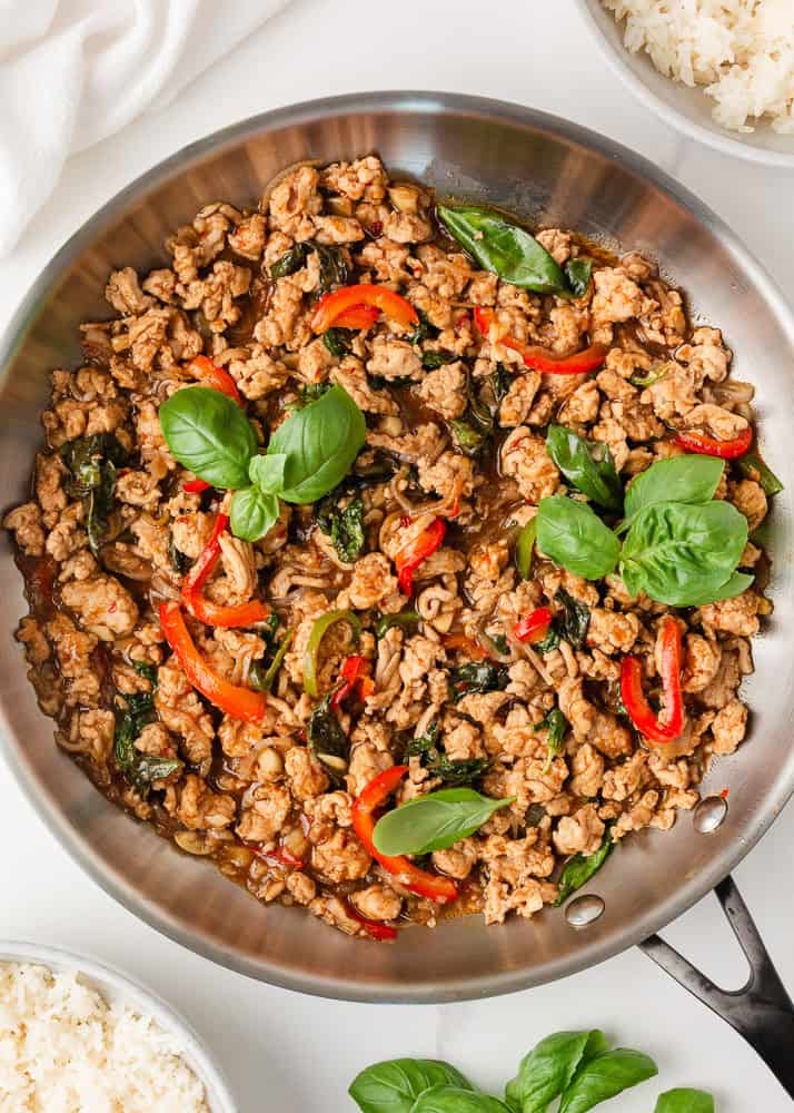 This easy Thai basil chicken recipe is bold, savory, and ready in under 30 minutes. It's everything you love about your favorite Thai food, made right at home! Thai basil chicken with ground chicken, basil leaves, and red chili peppers in skillet.