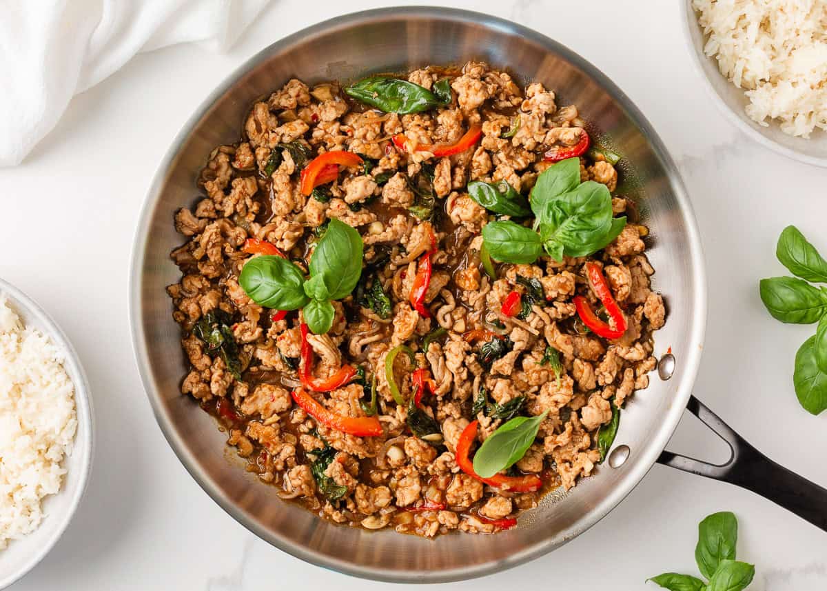 This easy Thai basil chicken recipe is bold, savory, and ready in under 30 minutes. It's everything you love about your favorite Thai food, made right at home! Thai basil chicken (pad krapow gai) in a skillet with ground chicken, red peppers, and fresh basil.