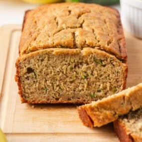 Easy zucchini banana bread loaf sliced on a cutting board with fresh zucchini and bananas.