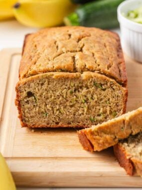 Easy zucchini banana bread loaf sliced on a cutting board with fresh zucchini and bananas.