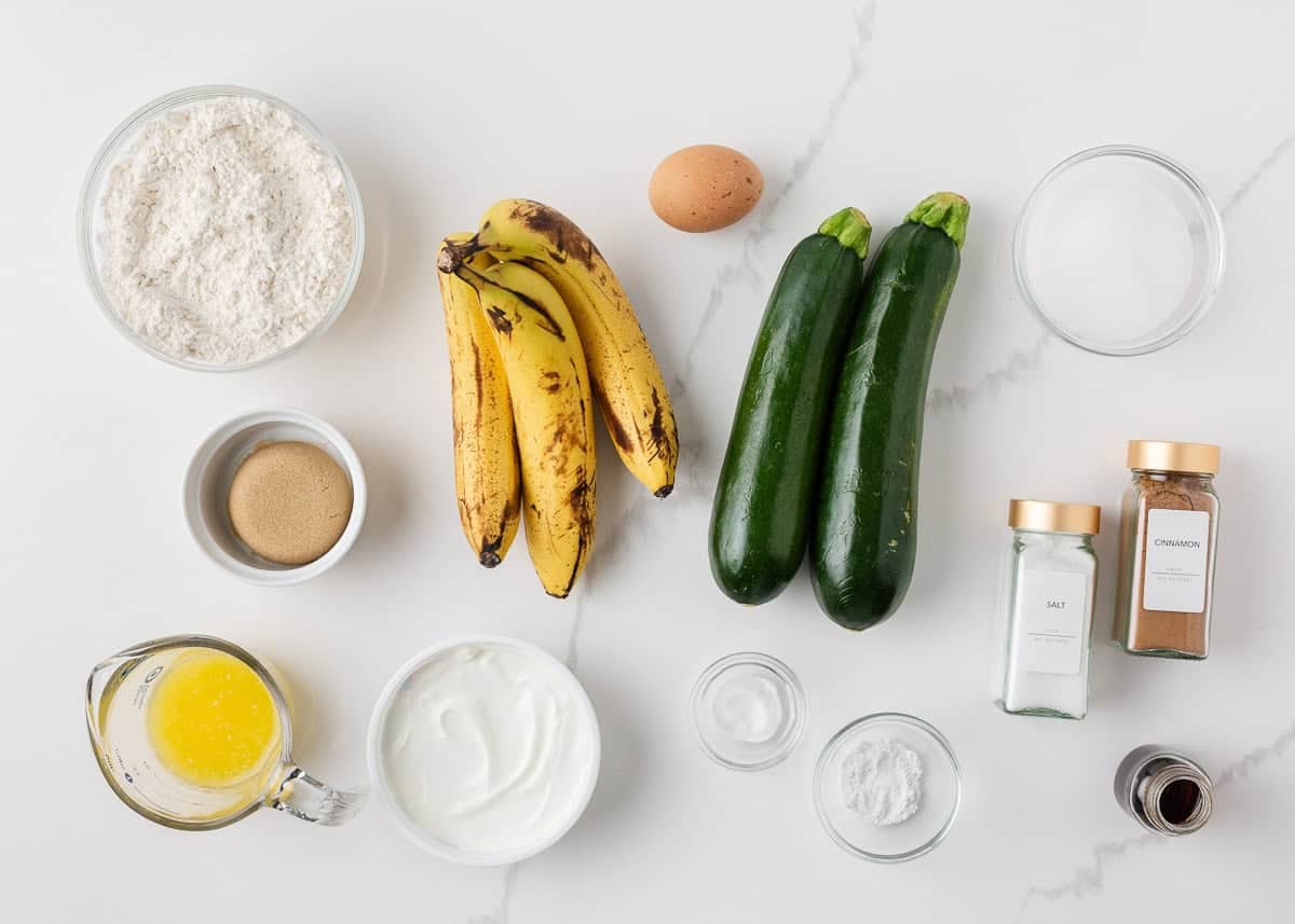 Moist, tender, and packed with flavor, this zucchini banana bread is a delicious way to use up ripe bananas and fresh zucchini in one easy loaf! Zucchini banana bread ingredients arranged on a counter with ripe bananas, zucchini, flour, egg, sour cream and cinnamon.