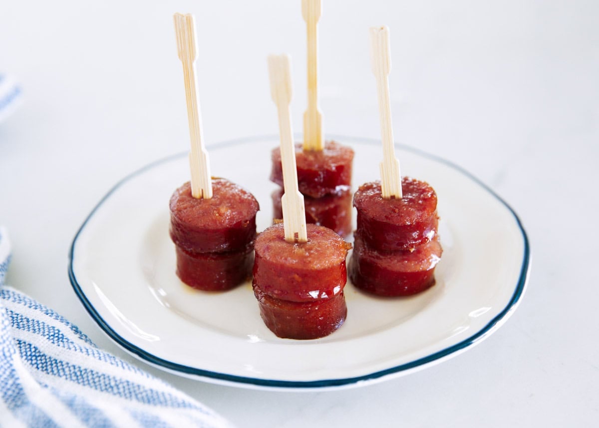 Brown sugar kielbasa bites served on a white plate with appetizer picks.