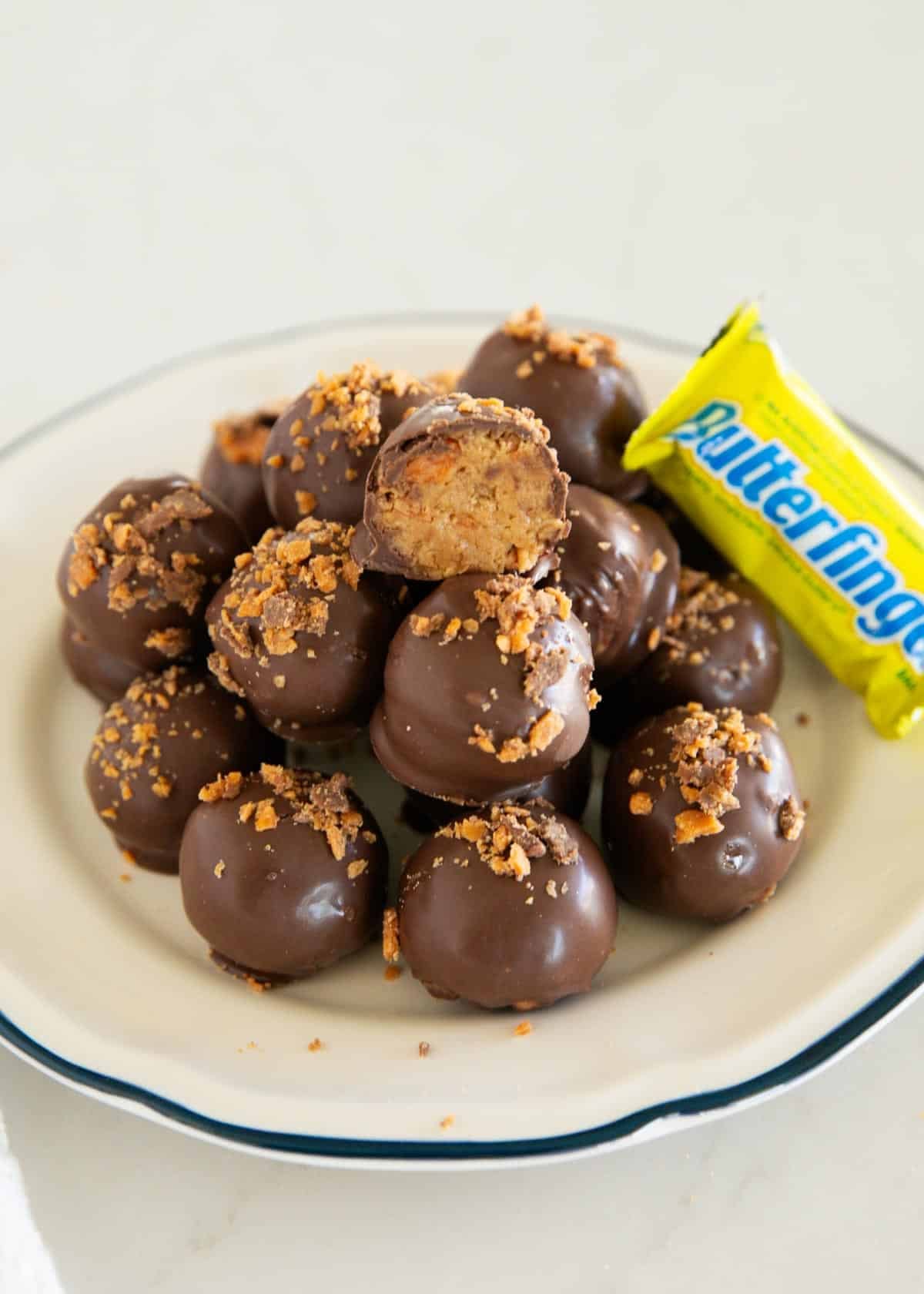 These Butterfinger balls are bite-sized no-bake truffles with crushed Butterfinger candy and graham crackers folded into the filling, then dipped in chocolate. An irresistible sweet treat! Butterfinger balls on a plate with one split in half to show candy center.