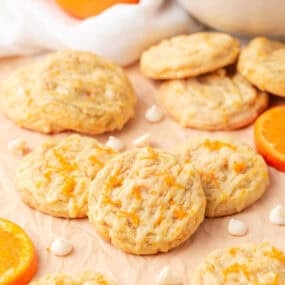 Homemade creamsicle orange cookies drizzled with glaze and topped with orange zest on parchment paper.