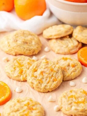 Homemade creamsicle orange cookies drizzled with glaze and topped with orange zest on parchment paper.
