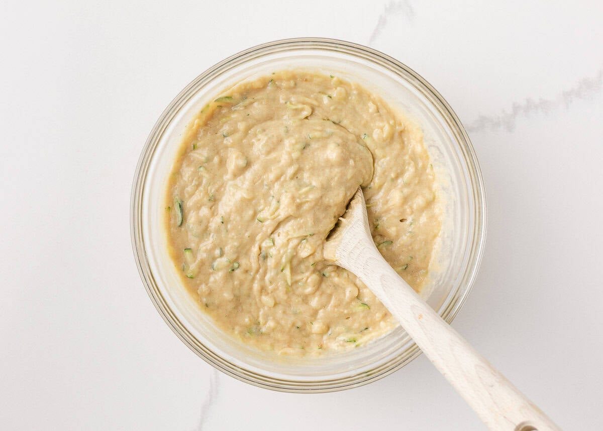 Moist, tender, and packed with flavor, this zucchini banana bread is a delicious way to use up ripe bananas and fresh zucchini in one easy loaf! Zucchini banana bread batter mixed together in a glass bowl with a wooden spoon.