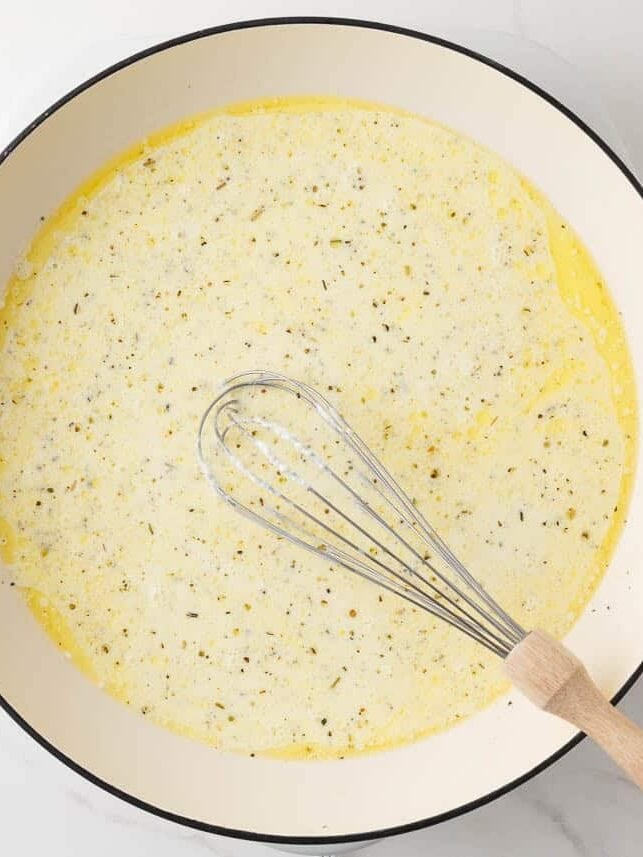 Alfredo sauce being whisked together in a large white skillet.