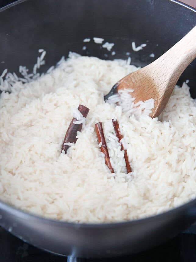 Rice and cinnamon sticks added to water in a large black pot.