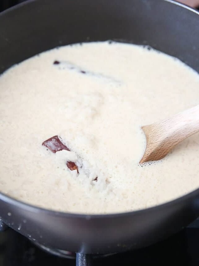 Milk mixture being stirred into cooked rice in a black pot on the stovetop.