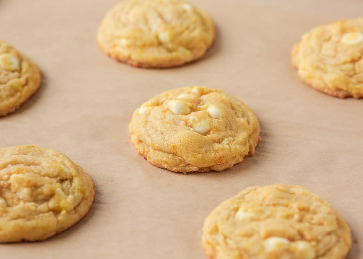 Freshly baked creamsicle orange cookies cooling on a parchment-lined baking sheet.
